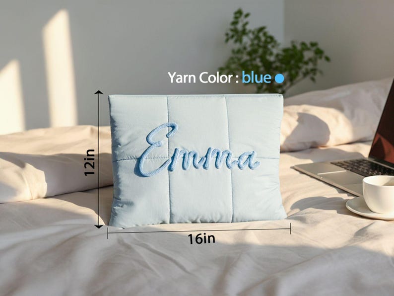 May include: A light blue, quilted pillow with the name "Emma" embroidered in blue script. The pillow measures 16 inches wide and 12 inches tall.
