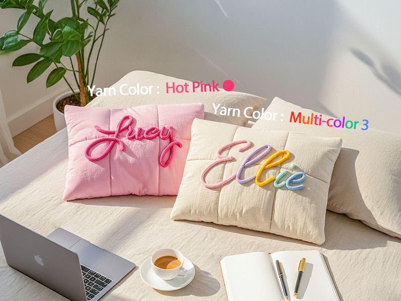 May include: Two decorative throw pillows with personalized names. One is pink with "Lucy" in hot pink yarn, the other is cream with "Ellie" in multi-colored yarn. The pillows are on a bed with a laptop and coffee.