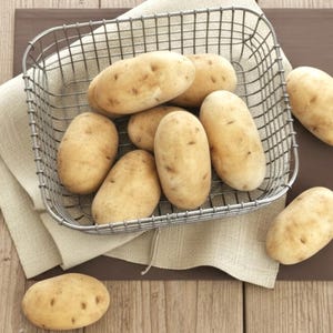 Peut inclure: Un panier en fil métallique rempli de plusieurs pommes de terre oblongues brun clair. Les pommes de terre reposent sur un tissu en lin beige. Quelques pommes de terre sont à l'extérieur du panier sur une surface en bois.