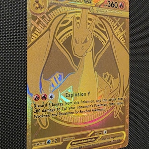 May include: A gold-colored Mega Charizard Y EX Pokémon card. The card features a detailed illustration of Charizard in a dynamic pose, with the text "Explosion Y" and other game details. The card is a Stage 2 evolution.