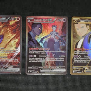 May include: Three Pokémon EX trading cards. The cards feature vibrant artwork of Pokémon characters and trainers. The cards have holographic effects and include text detailing abilities and attack power. The cards are displayed on a dark surface.
