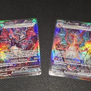 Könnte beinhalten: Zwei Charizard EX Pokémon-Sammelkarten. Die Karten haben ein holografisches Design mit einer feurigen Drachenillustration. Jede Karte zeigt den Text "Charizard EX" und "Infernal Reign". Die Karten haben 330 KP.