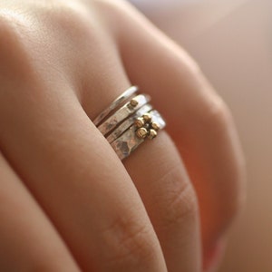 May include: A collection of silver rings with textured surfaces and small gold embellishments. The rings are worn on a finger, highlighting the contrast between the silver bands and the gold details. The rings are a piece of jewellery.