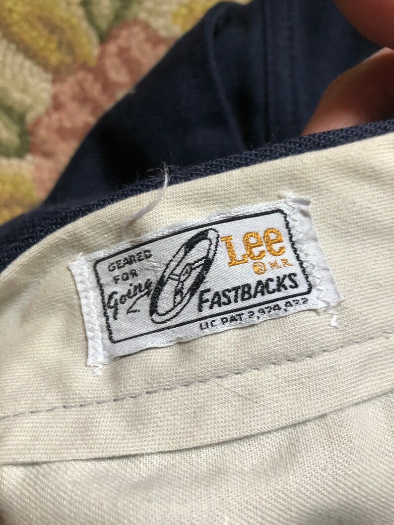 May include: A white label with blue and gold text and a graphic of a shoe. The label reads "Geared for Going Lee Fastbacks Lic Pat 2,978,422".