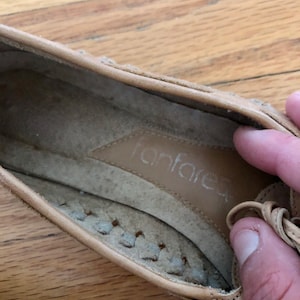 May include: Tan leather flat shoes with a braided detail around the toe and a leather insole with the word "fanfare" printed on it.