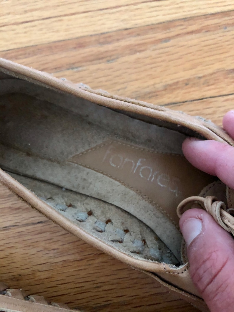 May include: Tan leather flat shoes with a braided detail around the toe and a leather insole with the word "fanfare" printed on it.