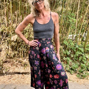 Könnte beinhalten: Ein anthrazitfarbenes, geripptes Trägershirt mit dünnen Trägern kombiniert mit einer schwarzen Culotte mit weitem Bein und einem sich wiederholenden geometrischen Muster in leuchtendem Lila, Pink, Orange und Grün. Die Hose hat eine hohe Taille.