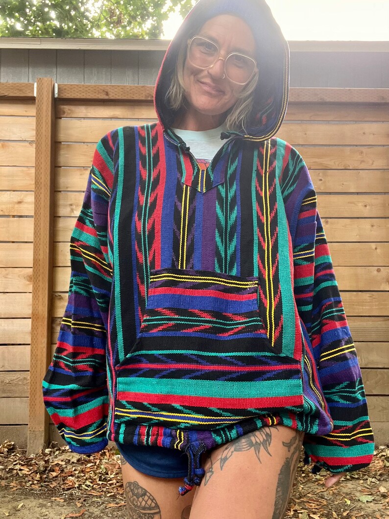 May include: A colourful striped hooded sweatshirt with a drawstring. The sweatshirt has a large pocket on the front and is made of a soft, woven fabric.