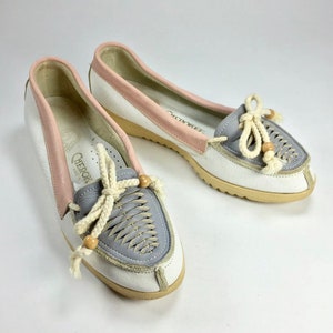 May include: A pair of white leather loafers with a gray and pink leather trim. The loafers have a rope lace with wooden beads and the brand name "Cherokee" is visible on the insole.