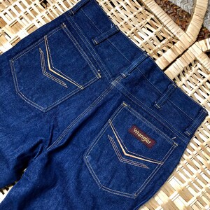 May include: A pair of dark blue denim jeans with a brown leather Wrangler label on the back pocket. The jeans have a classic five-pocket style and are made of a durable cotton blend.