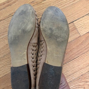 May include: A pair of tan leather woven flats with a rubber sole. The shoes are worn and have some dirt on the soles.