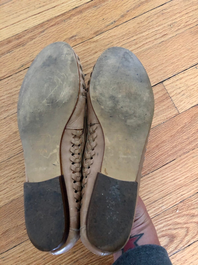May include: A pair of tan leather woven flats with a rubber sole. The shoes are worn and have some dirt on the soles.