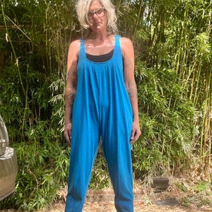 May include: A turquoise jumpsuit with a scoop neckline and wide straps. The one-piece garment has a loose, flowing fit and is adorned with small, dark blue polka dots. The model is wearing black shoes.