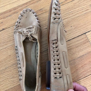 May include: A pair of beige leather shoes with a woven design. The shoes have a lace-up front and a rounded toe.