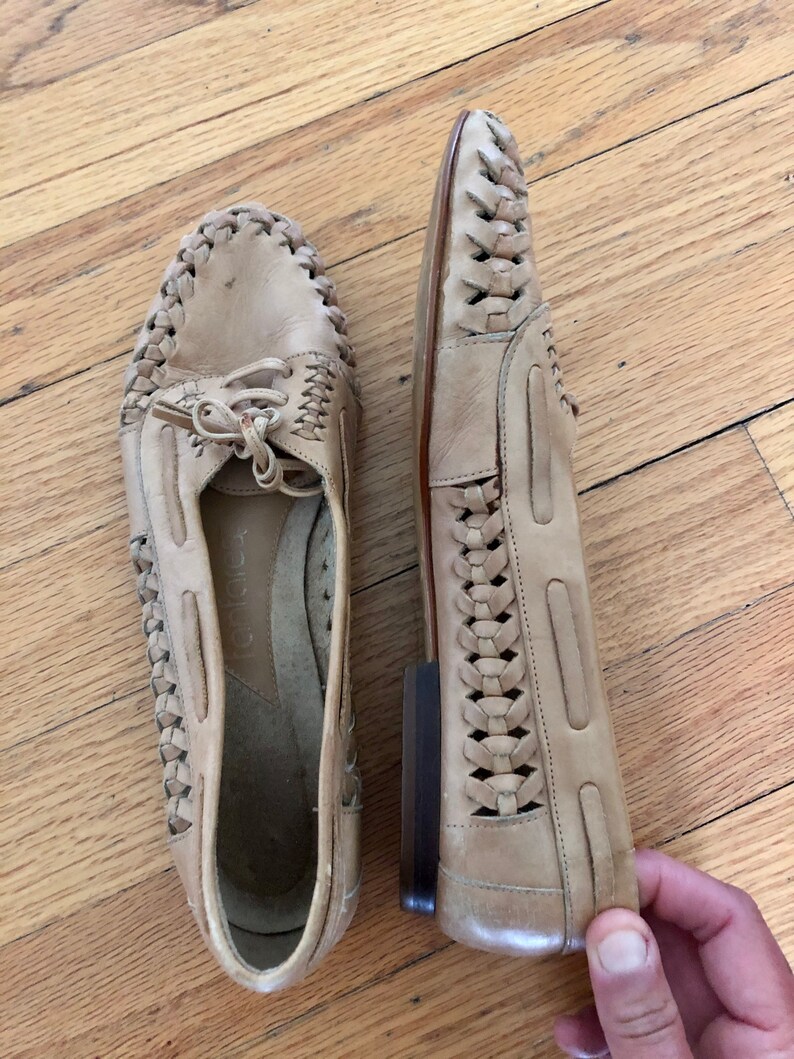 May include: A pair of beige leather shoes with a woven design. The shoes have a lace-up front and a rounded toe.