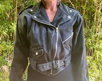 Pode incluir: Jaqueta de motociclista de ganga preta com gola de lapela, ombreiras e cinto. Possui fecho de correr frontal, dois bolsos frontais e punhos com zíper. Estilo clássico.