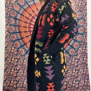 May include: A black cardigan with a colorful geometric pattern. The pattern includes shades of orange, red, purple, green, and yellow. The cardigan has a long, open front and long sleeves.