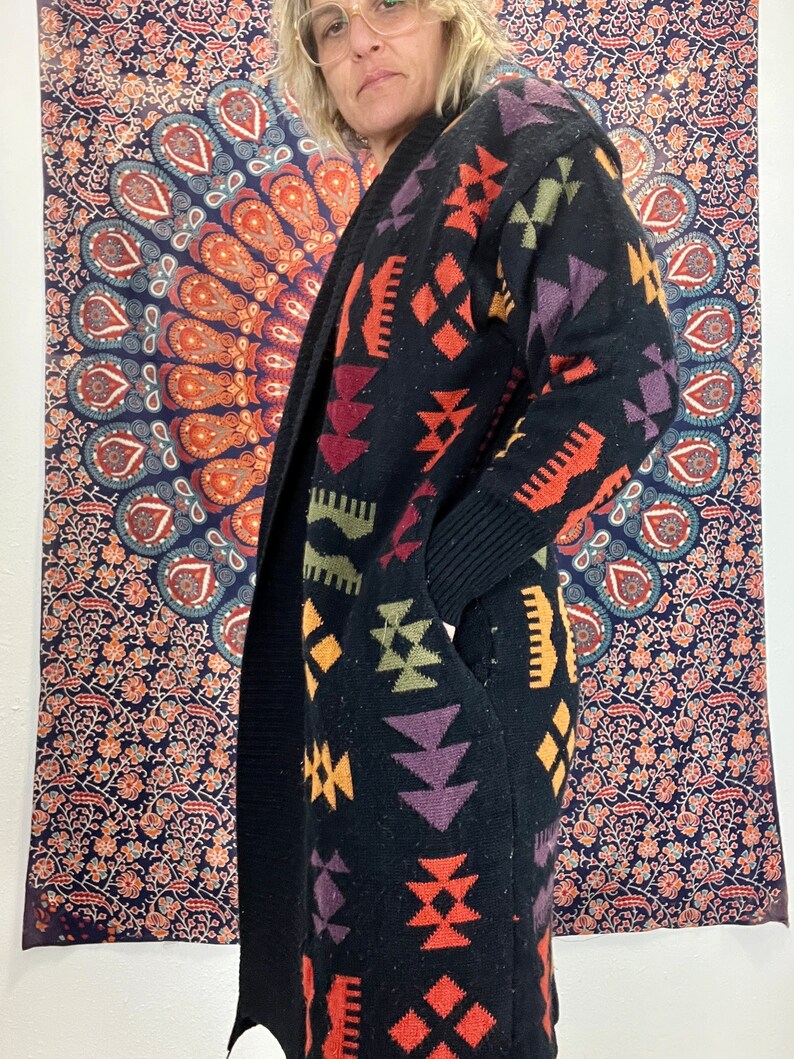 May include: A black cardigan with a colorful geometric pattern. The pattern includes shades of orange, red, purple, green, and yellow. The cardigan has a long, open front and long sleeves.