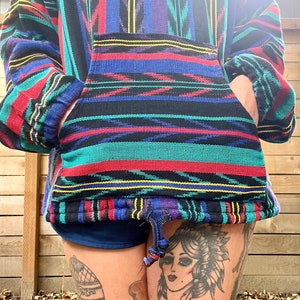 May include: A colourful, striped pullover with a drawstring hood. The pullover has a large pocket on the front and is made of a soft, woven fabric.