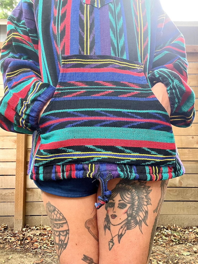 May include: A colourful, striped pullover with a drawstring hood. The pullover has a large pocket on the front and is made of a soft, woven fabric.
