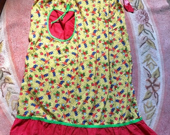 Könnte beinhalten: Eine vintage rote und gelbe Schürze mit grünem Besatz und einer roten Tasche. Die Schürze hat ein Muster aus kleinen roten Äpfeln und grünen Blättern auf gelbem Hintergrund.