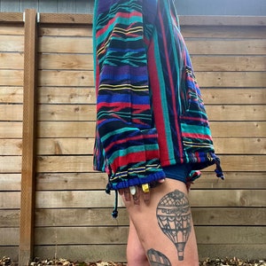 May include: A colourful striped jacket with a zip closure. The jacket is made of a soft, woven fabric. The person wearing the jacket has a tattoo of hot air balloons on their leg.