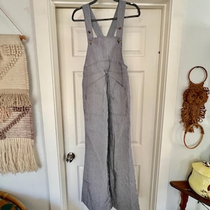 May include: A pair of black and white striped overalls with a wide leg, featuring a criss-cross strap design and button closures.