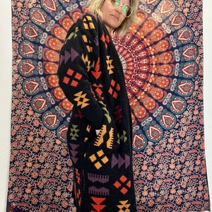 May include: A black long-sleeved cardigan with a geometric pattern in shades of orange, yellow, purple, and green. The cardigan has a shawl collar and a relaxed fit.