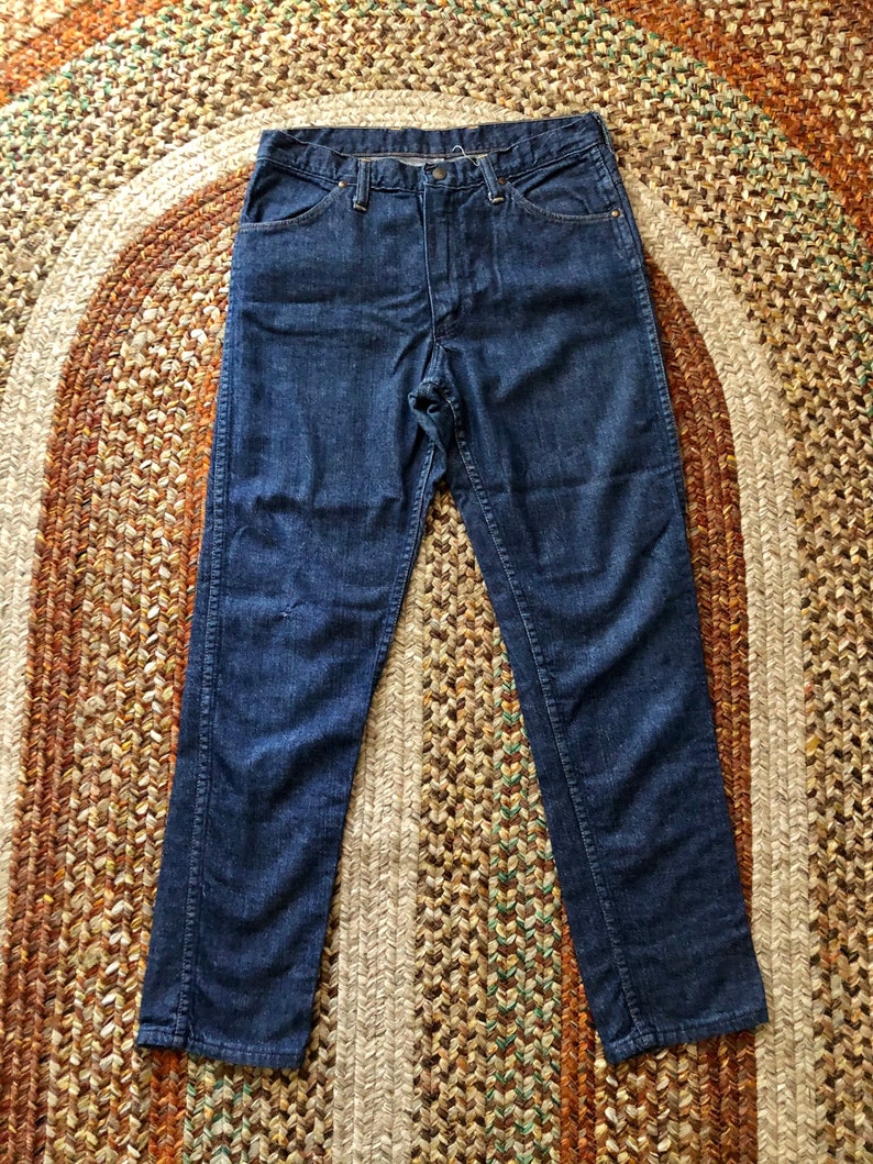 May include: A pair of dark blue denim jeans with a straight leg fit. The jeans have a button fly and five pockets.