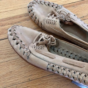 May include: A pair of beige leather shoes with a woven design. The shoes have laces and a tassel detail.