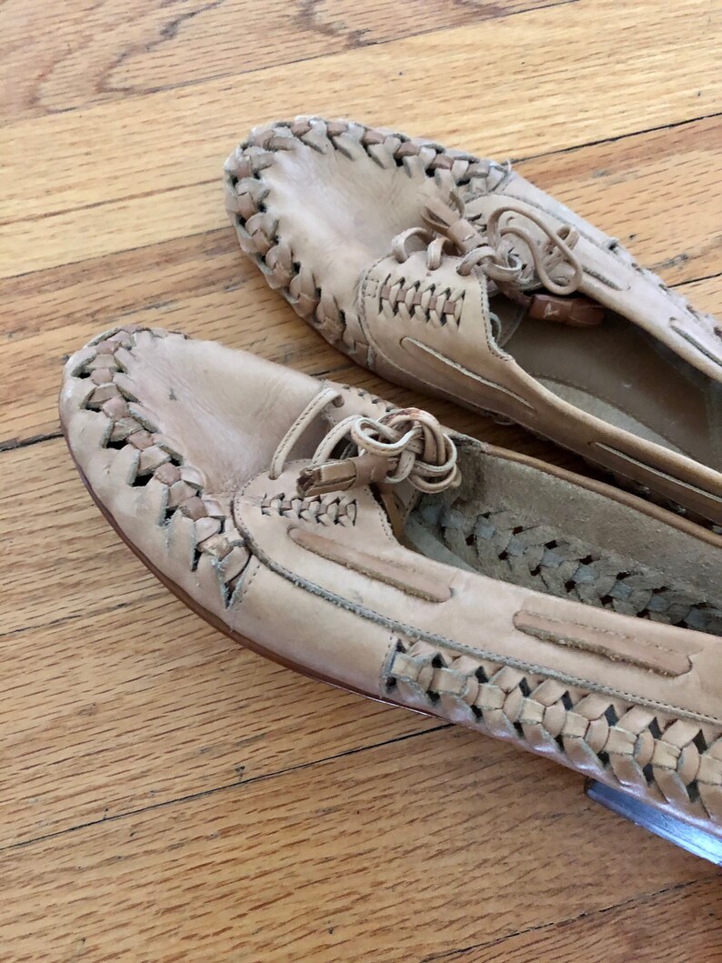 May include: A pair of beige leather shoes with a woven design. The shoes have laces and a tassel detail.