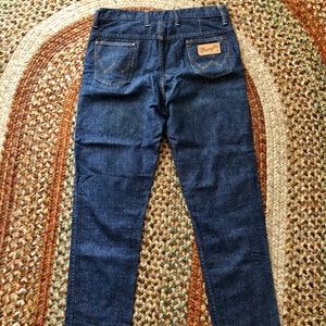 May include: A pair of dark blue denim jeans with a leather patch on the back pocket that says "Wrangler".