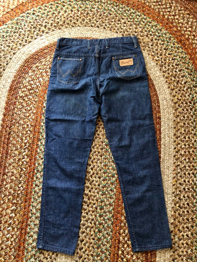 May include: A pair of dark blue denim jeans with a leather patch on the back pocket that says "Wrangler".