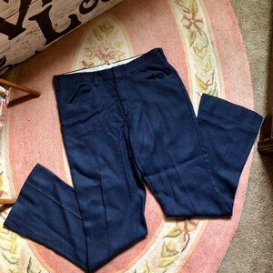 May include: A pair of dark blue, straight-leg pants with a slight flare at the bottom. The pants are made of a textured fabric and have a classic, timeless style.