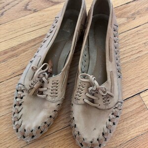 May include: A pair of tan leather shoes with woven detailing and laces. The shoes have a casual, comfortable style.