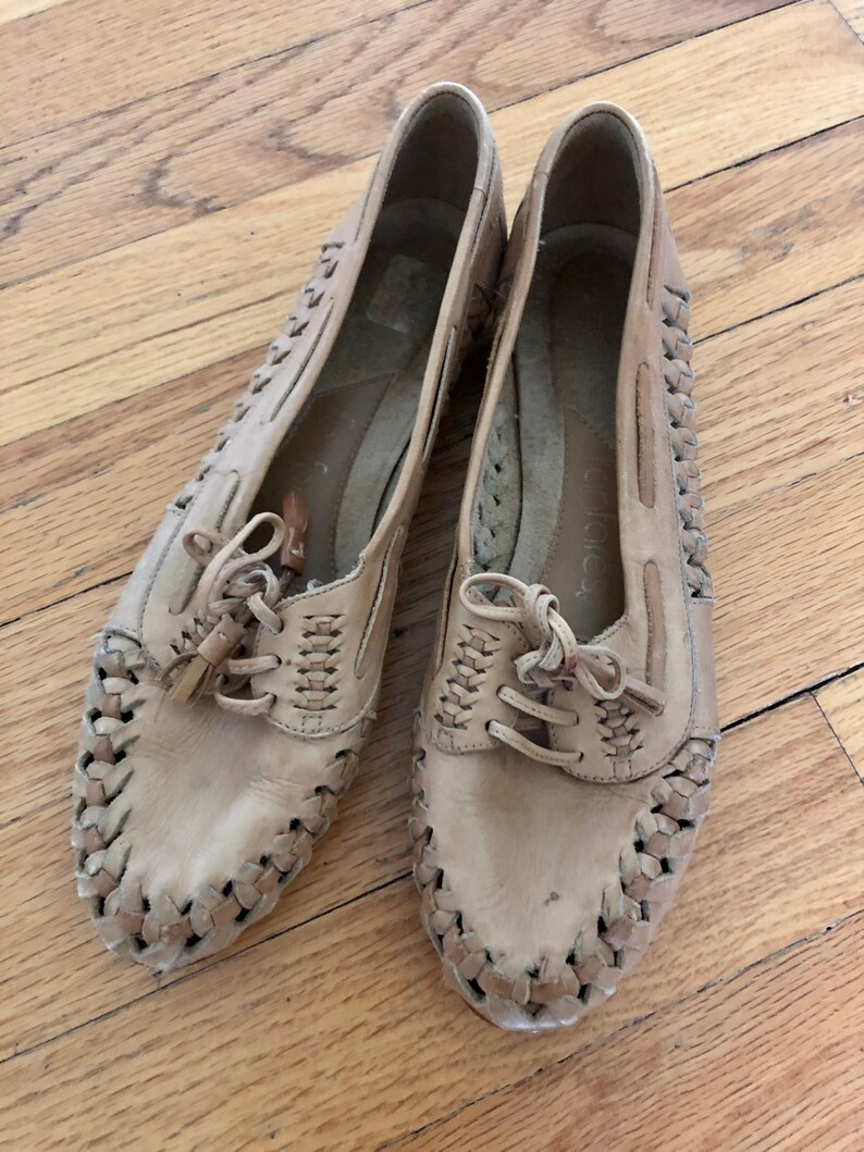 May include: A pair of tan leather shoes with woven detailing and laces. The shoes have a casual, comfortable style.