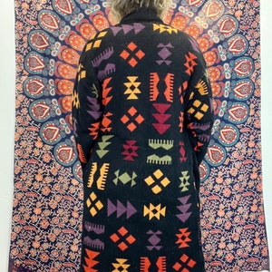 May include: A long black cardigan with a geometric pattern in shades of orange, yellow, red, purple, and green. The pattern is reminiscent of traditional Native American designs.