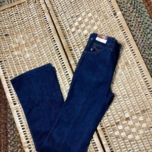 May include: A pair of dark blue denim jeans with a light brown woven background. The jeans have a straight leg and a classic five-pocket style.
