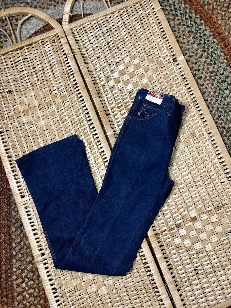 May include: A pair of dark blue denim jeans with a light brown woven background. The jeans have a straight leg and a classic five-pocket style.