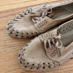 May include: A pair of tan leather shoes with woven detailing and laces. The shoes have a tassel accent on the laces.