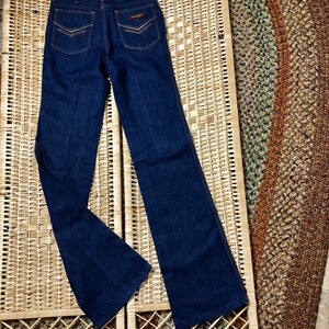 May include: A pair of dark blue denim jeans with a wide leg and a flared bottom. The jeans have a brown leather patch on the back with the word "Wrangler" written on it.