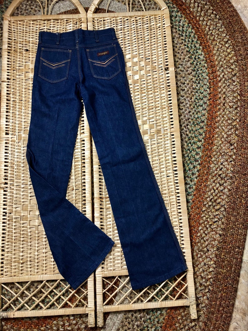 May include: A pair of dark blue denim jeans with a wide leg and a flared bottom. The jeans have a brown leather patch on the back with the word "Wrangler" written on it.