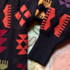 May include: A black sweater with a colorful geometric pattern. The sweater has a ribbed cuff and is made of a soft, knitted fabric.