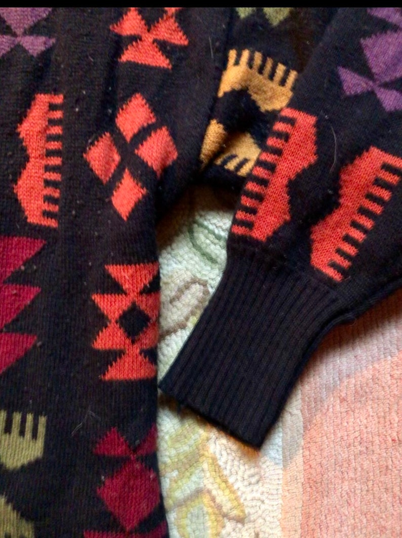 May include: A black sweater with a colorful geometric pattern. The sweater has a ribbed cuff and is made of a soft, knitted fabric.