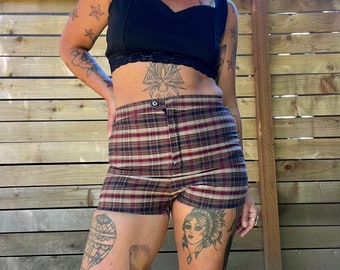 Peut inclure: Une femme portant un haut court noir avec une bordure en dentelle et un short à carreaux brun et blanc. Elle a plusieurs tatouages sur les bras et les jambes.