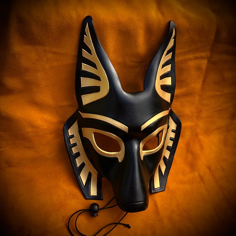 May include: A black leather mask with gold accents, shaped like an animal head with pointed ears. The mask has a detailed design with geometric patterns and a long snout.