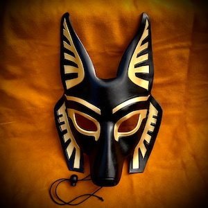 May include: Black leather mask with gold accents, shaped like an animal head with pointed ears. The mask has eye holes and a small nose.