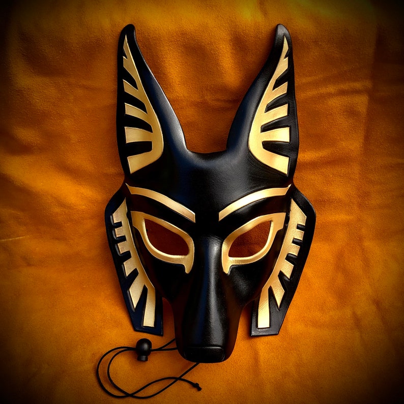 May include: Black leather mask with gold accents, shaped like an animal head with pointed ears. The mask has eye holes and a small nose.