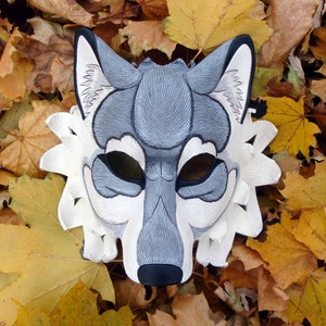 Op de afbeelding: Een handgemaakt wolfsmasker in grijstinten, zwart en wit, met ingewikkelde details. Het masker is geplaatst tegen een achtergrond van herfstbladeren, wat het ontwerp benadrukt. Geschikt voor kostuumfeesten of theatervoorstellingen.
