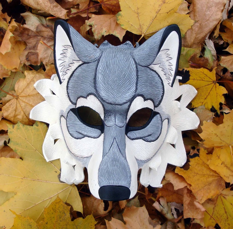 Op de afbeelding: Een handgemaakt wolfsmasker in grijstinten, zwart en wit, met ingewikkelde details. Het masker is geplaatst tegen een achtergrond van herfstbladeren, wat het ontwerp benadrukt. Geschikt voor kostuumfeesten of theatervoorstellingen.